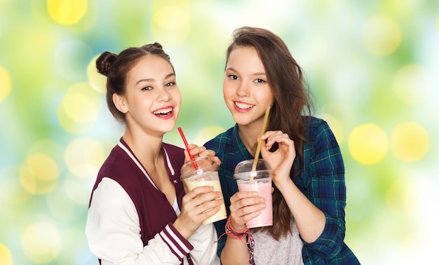 concept de personnes, d'amis, d'adolescents et d'amitié - jolies adolescentes souriantes et heureuses buvant des milk-shakes et avec de la paille sur fond de lumières de vacances vertes