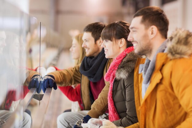 concept de personnes, d'amitié, de sport et de loisirs - amis heureux regardant un match de hockey ou une performance de patinage artistique sur une patinoire