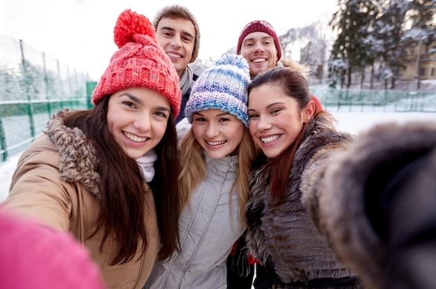 concept de personnes, d'amitié, de technologie, d'hiver et de loisirs - amis heureux prenant un selfie avec un smartphone ou un appareil photo à l'extérieur