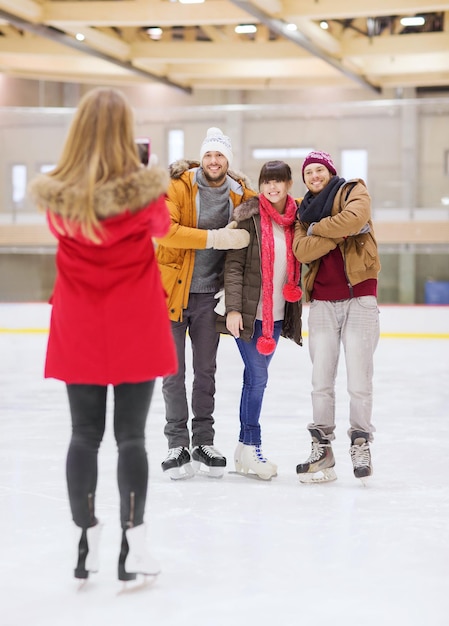 concept de personnes, d'amitié, de technologie et de loisirs - amis heureux prenant des photos avec un smartphone sur une patinoire