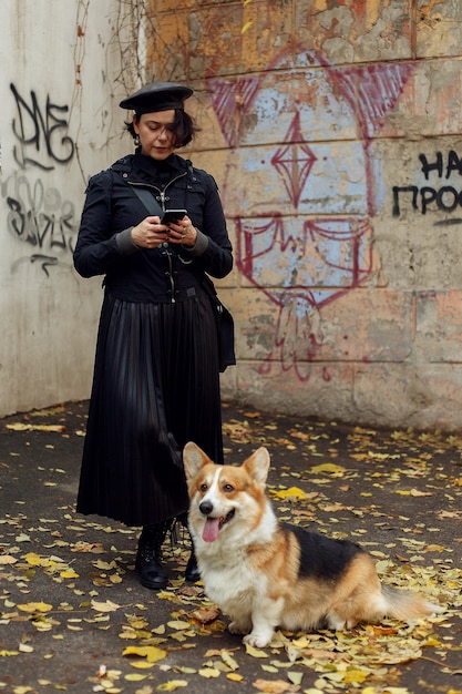 Concept de personnes, d'animaux, de beauté, de mode, de mode de vie et de couleur - Portrait complet du corps en plein air d'une belle jeune fille souriante et heureuse posant dans la rue. fille avec chien corgi. Dame portant des vêtements élégants