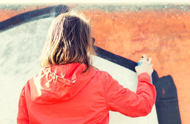 concept de personnes, d'art, de créativité et de culture des jeunes - jeune femme ou adolescente dessinant des graffitis avec de la peinture en aérosol sur le mur de la rue de l'arrière