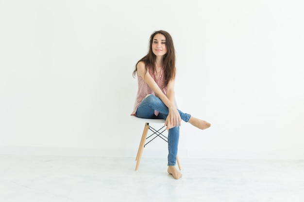 Concept de personnes, de beauté et de mode - jeune femme brune posant sur une chaise isolée sur blanc