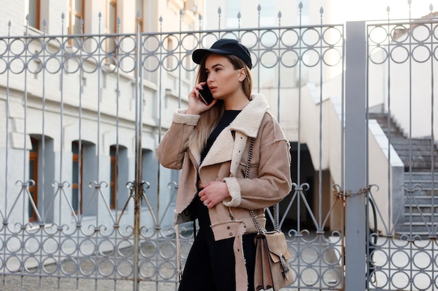 Concept de personnes, de beauté, de mode, de style de vie et de couleur - Portrait complet du corps en plein air d'une belle jeune fille souriante heureuse posant dans la rue. Modèle regardant la caméra. Fille textos sur le téléphone intelligent