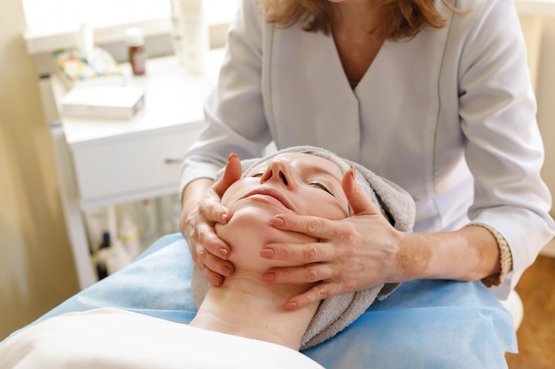 Concept de personnes, de beauté, de spa, de cosmétologie et de technologie - Belle jeune femme recevant un massage du visage les yeux fermés dans un salon de spa