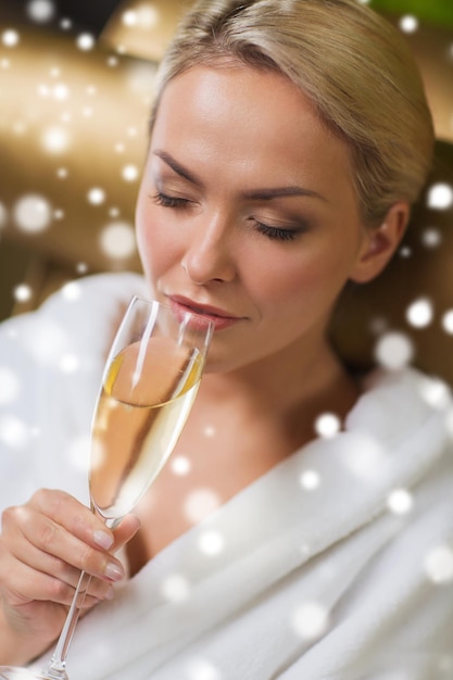 Photo concept de personnes, de beauté, de style de vie, de vacances et de détente - belle jeune femme en peignoir blanc buvant du champagne au spa avec effet de neige