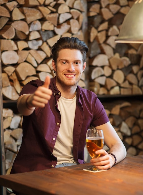 concept de personnes, de boissons, d'alcool, de gestes et de loisirs - jeune homme heureux buvant de la bière et montrant les pouces vers le haut au bar ou au pub