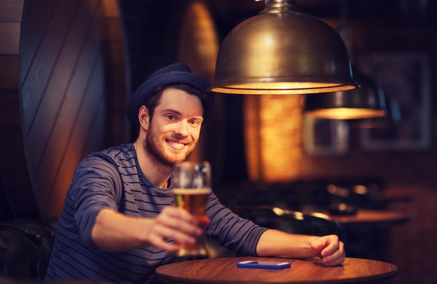 Photo concept de personnes, de boissons, d'alcool et de loisirs - jeune homme heureux buvant de la bière au bar ou au pub