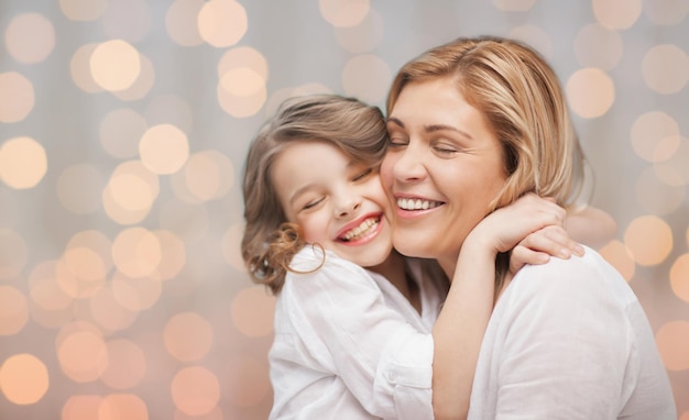 concept de personnes, de bonheur, d'amour, de famille et de maternité - heureuse mère et fille étreignant sur fond de lumières de vacances