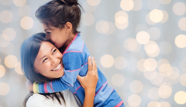 concept de personnes, de bonheur, d'amour, de famille et de maternité - heureuse mère et fille étreignant sur fond de lumières de vacances