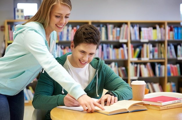 concept de personnes, de connaissances, d'éducation et d'école - étudiants heureux avec un livre se préparant aux examens en bibliothèque