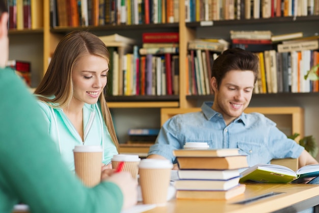 concept de personnes, de connaissances, d'éducation et d'école - groupe d'étudiants heureux lisant des livres, buvant du café et se préparant à l'examen en bibliothèque