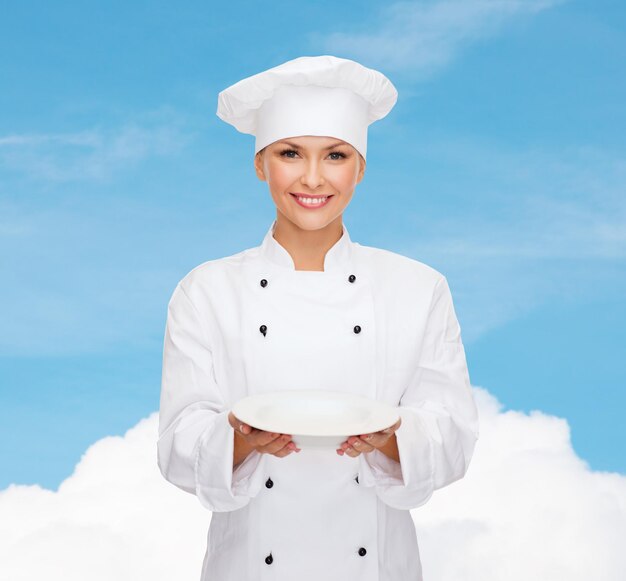 concept de personnes, de cuisine et de nourriture - chef féminin souriant, cuisinier ou boulanger avec assiette vide sur ciel bleu avec fond de nuage