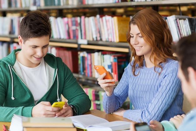 concept de personnes, d'éducation, de technologie et d'école - groupe d'étudiants heureux avec des smartphones et des livres envoyant des SMS ou en réseau dans la bibliothèque
