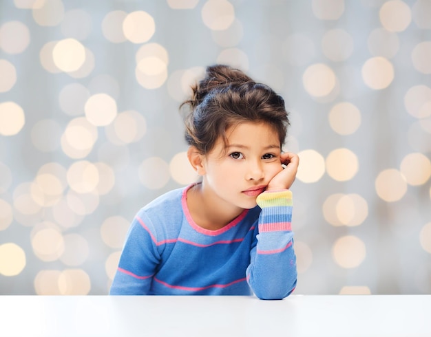 concept de personnes, d'enfance et d'émotions - petite fille triste sur fond de lumières de vacances