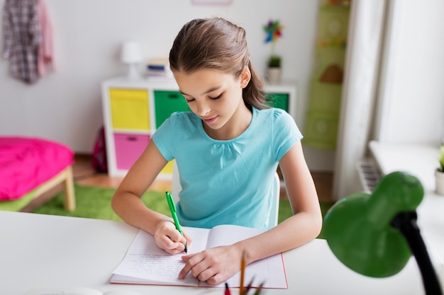 concept de personnes, d'enfants, d'éducation et d'apprentissage - fille heureuse écrivant sur un cahier à la maison