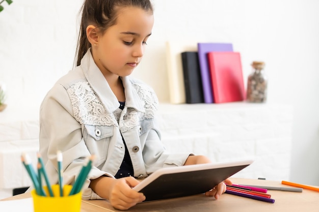 concept de personnes, d'enfants et d'éducation - fille avec un ordinateur tablette écrivant à la maison