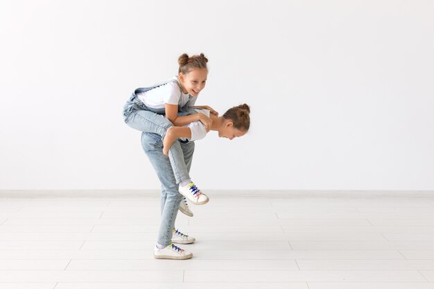 Concept de personnes, d'enfants et de famille - petite fille portant sa sœur jumelle sur fond blanc.