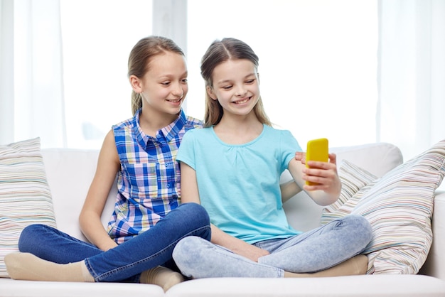 concept de personnes, d'enfants, de technologie, d'amis et d'amitié - petites filles heureuses assises sur un canapé et prenant un selfie avec un smartphone à la maison