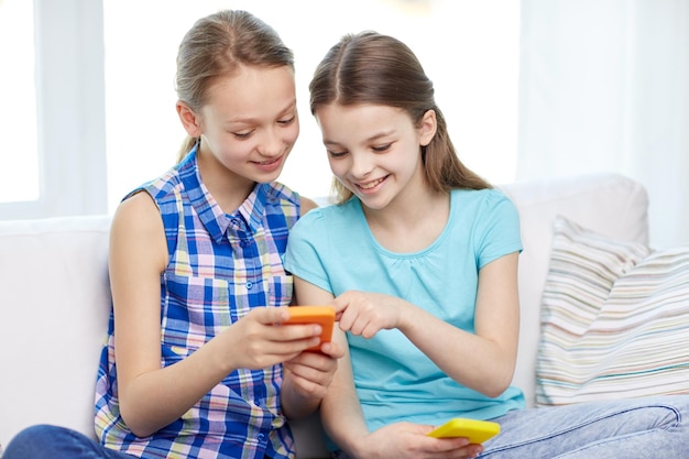 concept de personnes, d'enfants, de technologie, d'amis et d'amitié - petites filles heureuses avec des smartphones assis sur un canapé à la maison