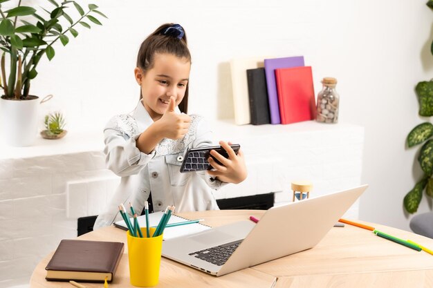 concept de personnes, d'enfants et de technologie - fille avec ordinateur portable et smartphone prenant un selfie ou ayant un appel vidéo à la maison