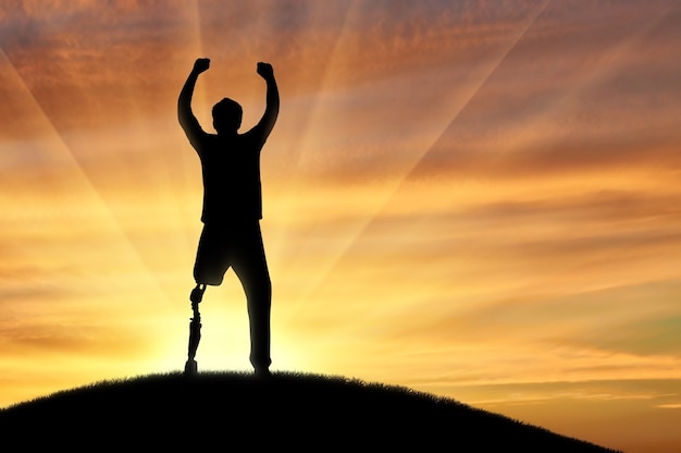 Photo concept de personnes handicapées. heureux homme handicapé avec une jambe prothétique debout au sommet d'une colline au coucher du soleil