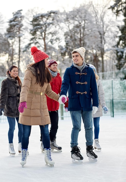 concept de personnes, d'hiver, d'amitié, de sport et de loisirs - amis heureux patinant sur la patinoire à l'extérieur