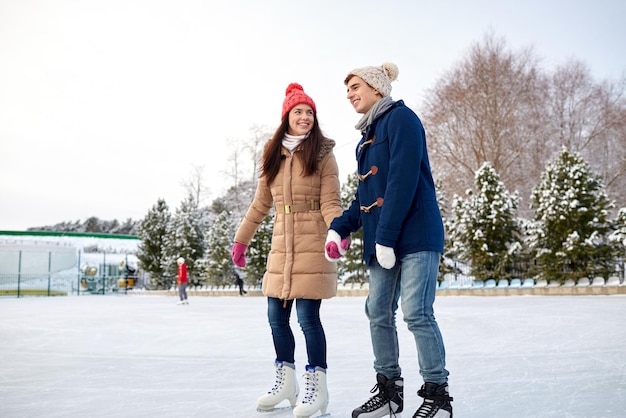 concept de personnes, d'hiver, d'amitié, de sport et de loisirs - couple heureux patinant sur la patinoire à l'extérieur