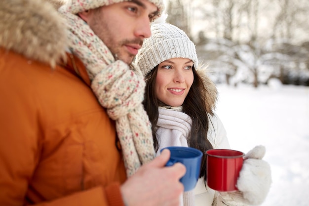 concept de personnes, d'hiver, de boissons et de saison - gros plan d'un couple heureux tenant des tasses de thé chaudes