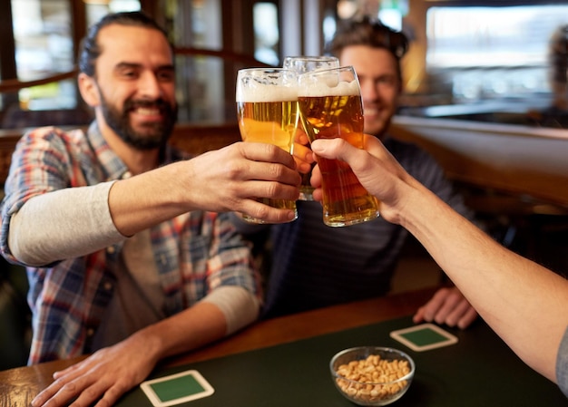 Concept de personnes, hommes, loisirs, amitié et célébration - heureux amis masculins, boire de la bière et tinter des verres au bar ou au pub