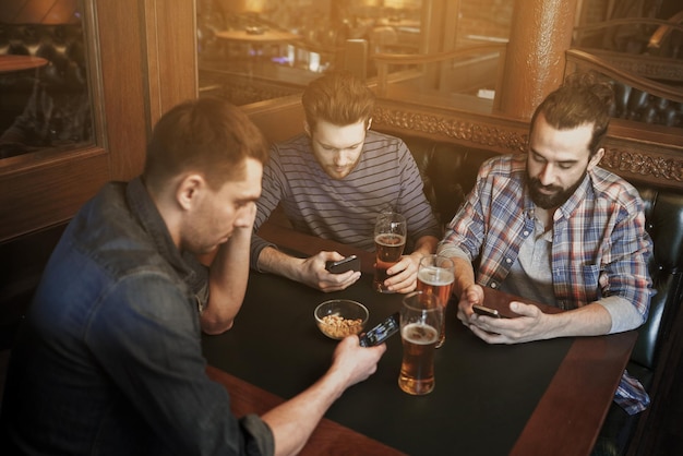 concept de personnes, d'hommes, de loisirs, d'amitié et de communication - amis masculins avec des smartphones buvant de la bière pression au bar ou au pub