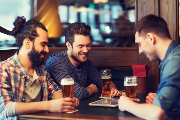 concept de personnes, d'hommes, de loisirs, d'amitié et de technologie - amis masculins heureux avec ordinateur tablette buvant de la bière au bar ou au pub