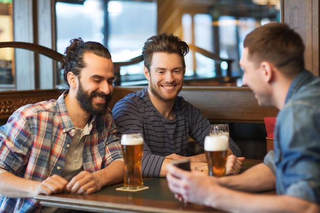 concept de personnes, d'hommes, de loisirs, d'amitié et de technologie - amis masculins heureux avec smartphone buvant de la bière au bar ou au pub