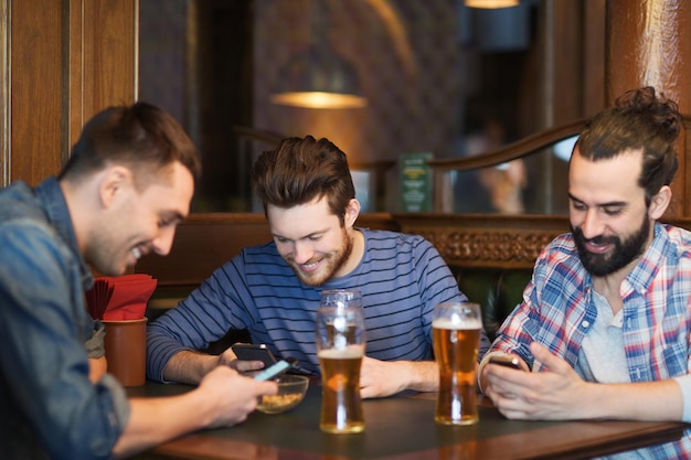 concept de personnes, d'hommes, de loisirs, d'amitié et de technologie - amis masculins heureux avec des smartphones buvant de la bière au bar ou au pub