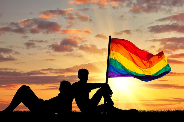 Concept De Personnes Homosexuelles. Silhouette De Deux Vacanciers Gays Au Coucher Du Soleil Et Drapeau Arc-en-ciel