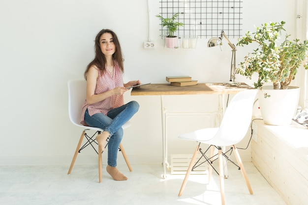 Concept de personnes, intérieur et technologie - jeune femme assise à une table avec tablette numérique dans la chambre