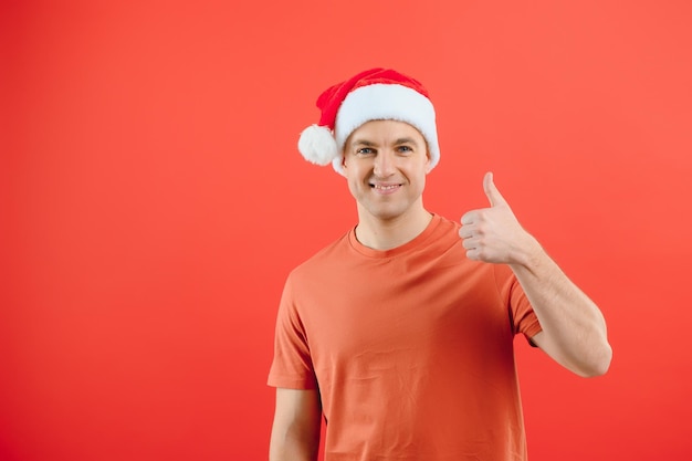 Concept personnes langage corporel approbation recommandationan homme excité chapeau de père Noël isolé sur fond de studio rouge avec espace pour le texte