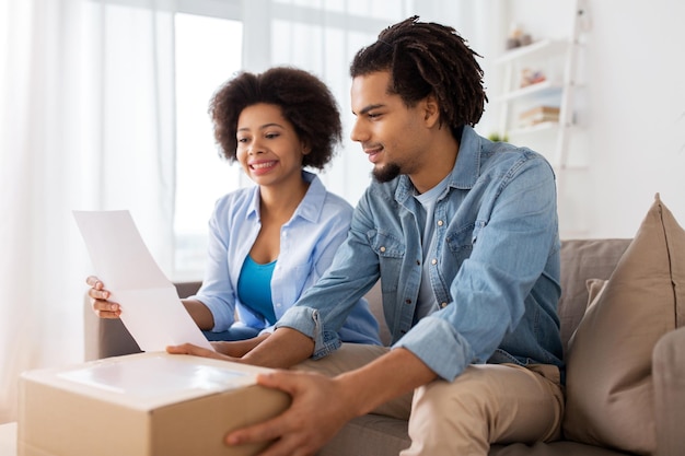 concept de personnes, de livraison et de consommation - couple heureux avec boîte à colis et formulaire papier à la maison