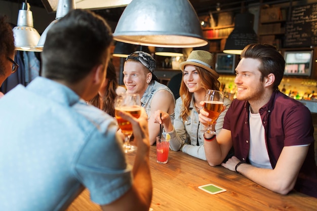 concept de personnes, de loisirs, d'amitié et de communication - groupe d'amis souriants heureux buvant de la bière et des cocktails parlant au bar ou au pub