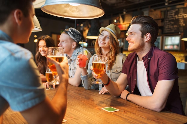 concept de personnes, de loisirs, d'amitié et de communication - groupe d'amis souriants heureux buvant de la bière et des cocktails parlant au bar ou au pub