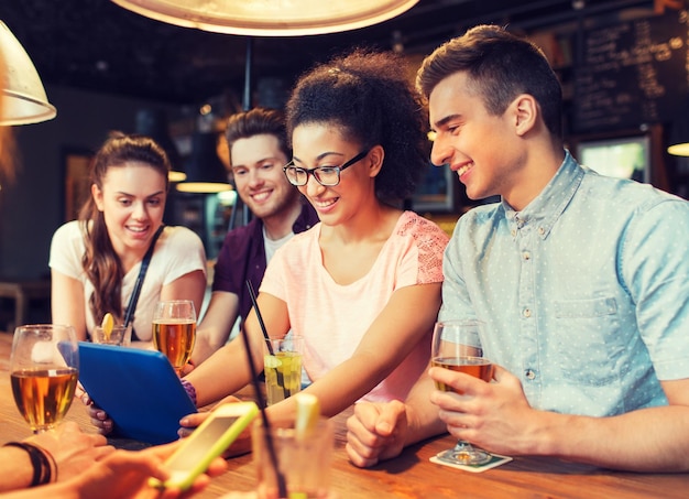 concept de personnes, de loisirs, d'amitié et de communication - groupe d'amis souriants heureux avec un ordinateur tablette et des boissons au bar ou au pub