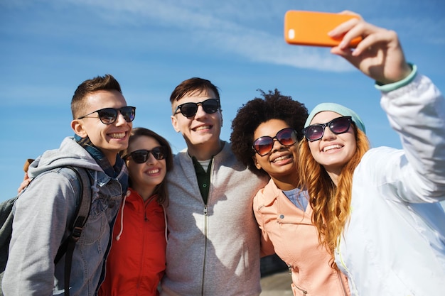 concept de personnes, de loisirs, d'amitié et de technologie - groupe d'amis adolescents souriants prenant un selfie avec un smartphone à l'extérieur