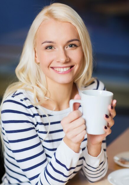 concept de personnes, loisirs, manger et boire - jeune femme heureuse buvant du thé ou du café au café ou à la maison