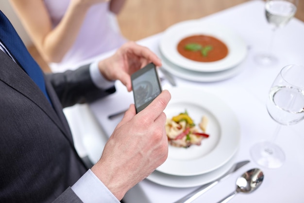 concept de personnes, de loisirs, de restauration et de technologie - gros plan d'un couple avec des smartphones prenant des photos de nourriture au restaurant