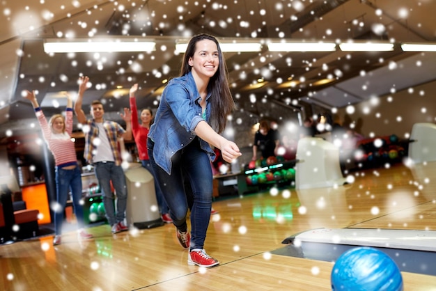 concept de personnes, de loisirs, de sport et de divertissement - jeune femme heureuse lançant une balle dans un club de bowling en hiver