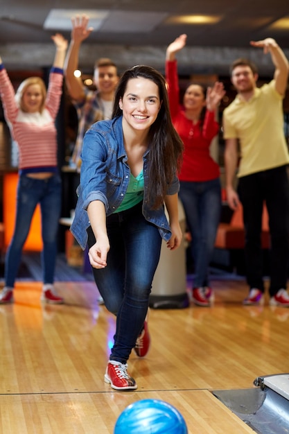 concept de personnes, de loisirs, de sport et de divertissement - jeune femme heureuse lançant une balle dans un club de bowling