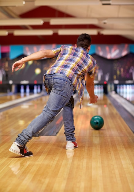 Photo concept de personnes, de loisirs, de sport et de divertissement - jeune homme heureux lançant une balle dans un club de bowling