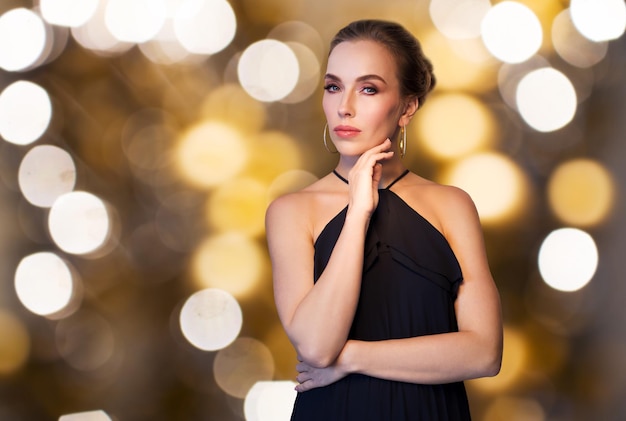 concept de personnes, de luxe, de bijoux et de vacances - belle femme en noir portant une boucle d'oreille en diamant et une bague sur fond de lumières