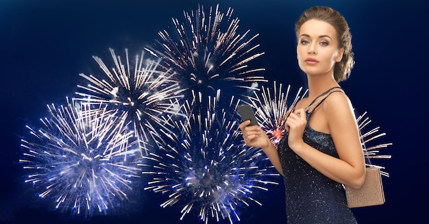 concept de personnes, de luxe, de vie nocturne et de finance - belle femme en robe de soirée avec carte vip et sac sur feu d'artifice sur fond bleu foncé