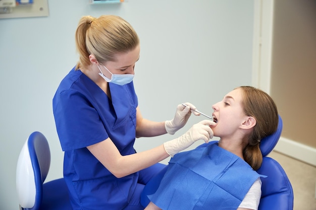 concept de personnes, de médecine, de stomatologie et de soins de santé - femme dentiste heureuse avec miroir vérifiant les dents de la patiente au bureau de la clinique dentaire